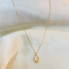 Gold necklace with a teardrop-shaped pendant on a white fabric background