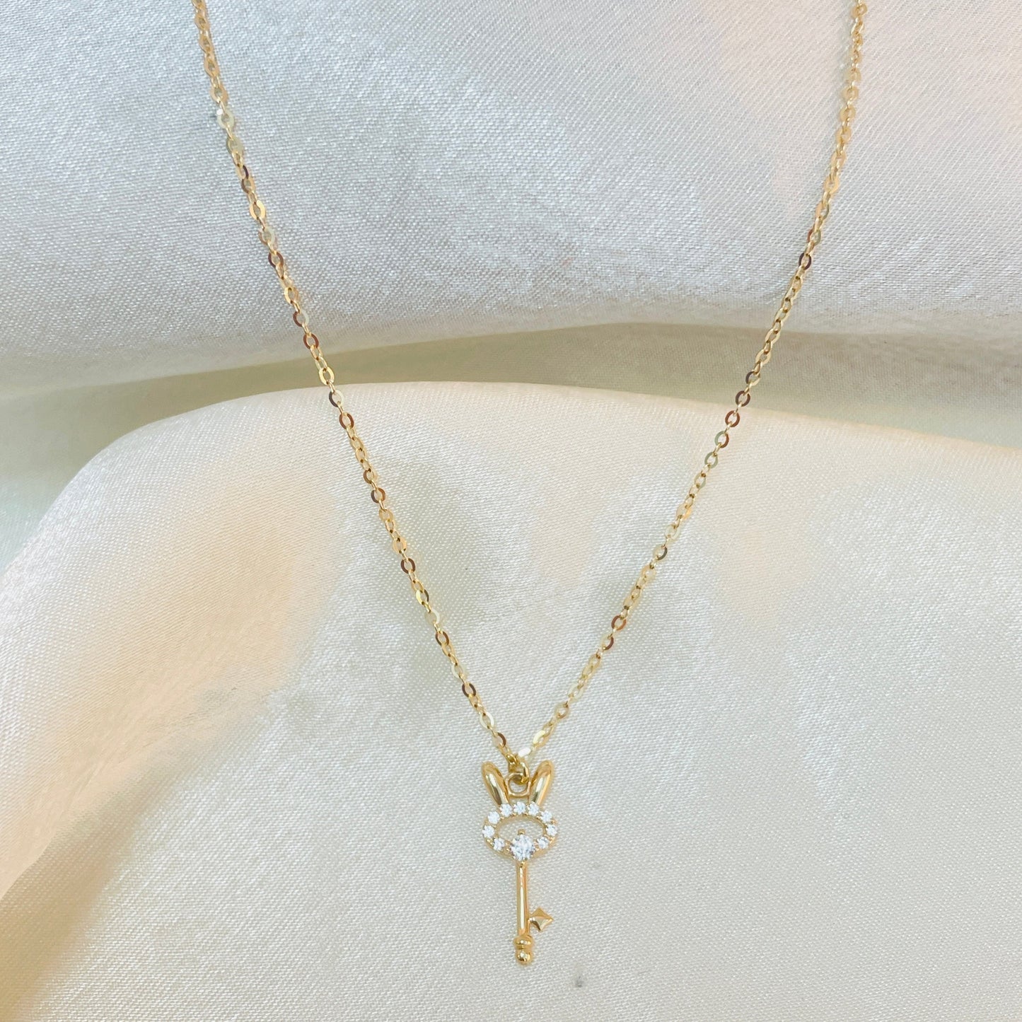 Gold key-shaped necklace with a small pendant on a white surface