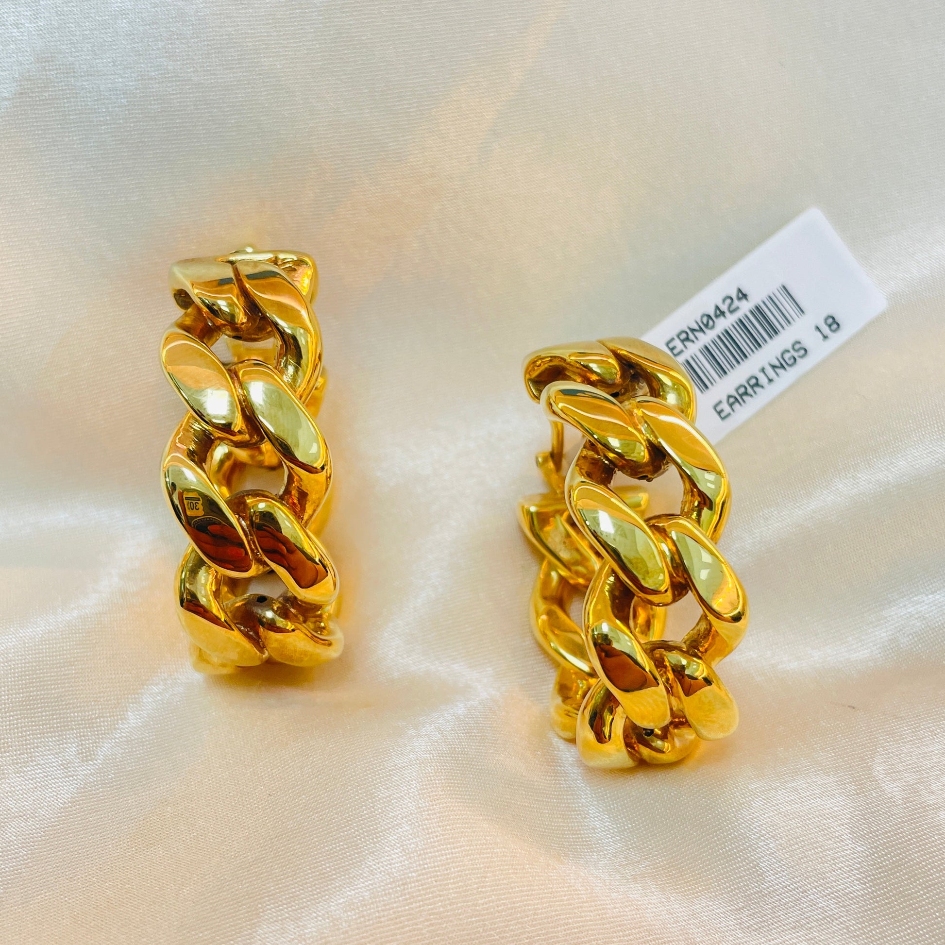 Pair of gold chain earrings on a white fabric background with a visible tag.