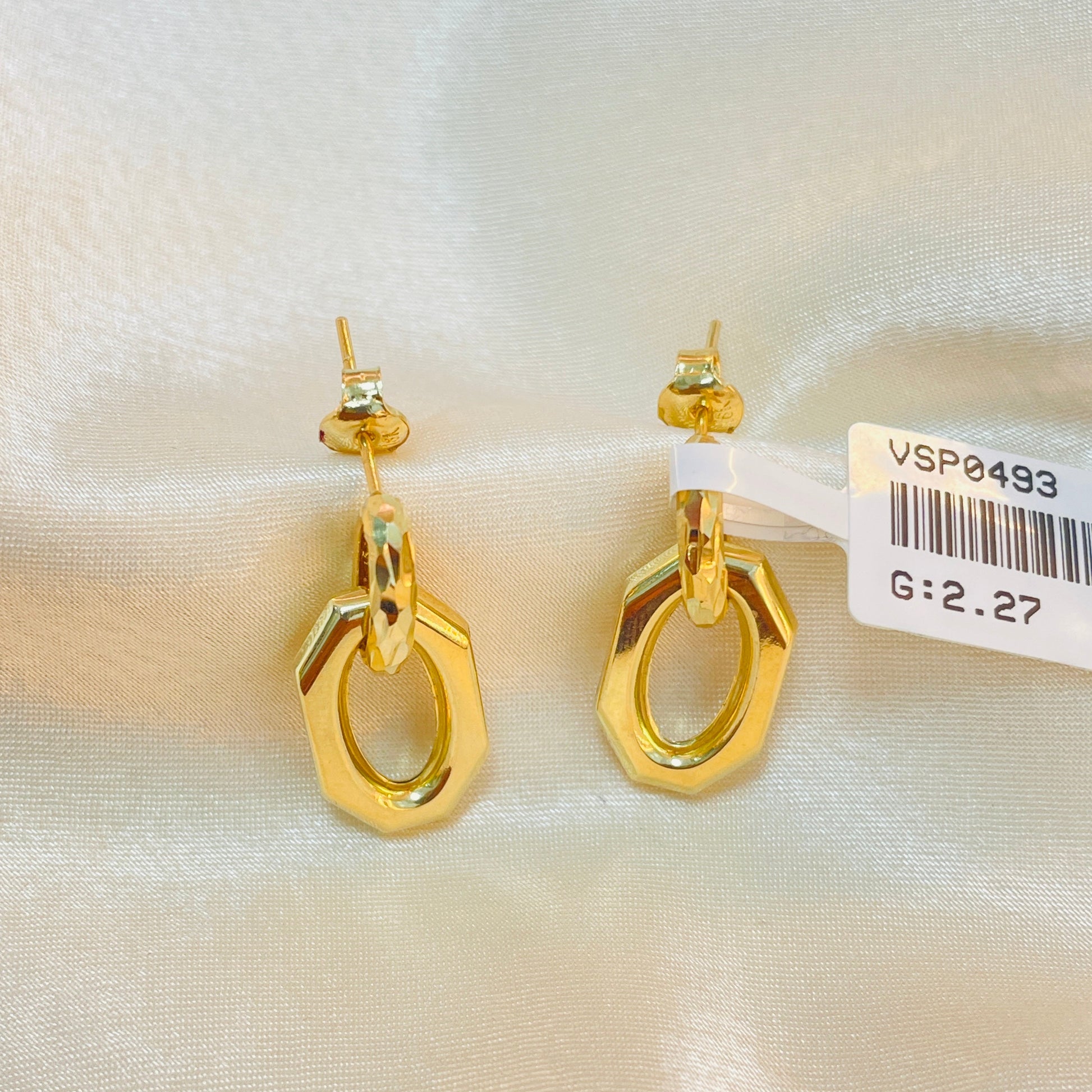 Gold earrings on a white fabric background with a visible tag.