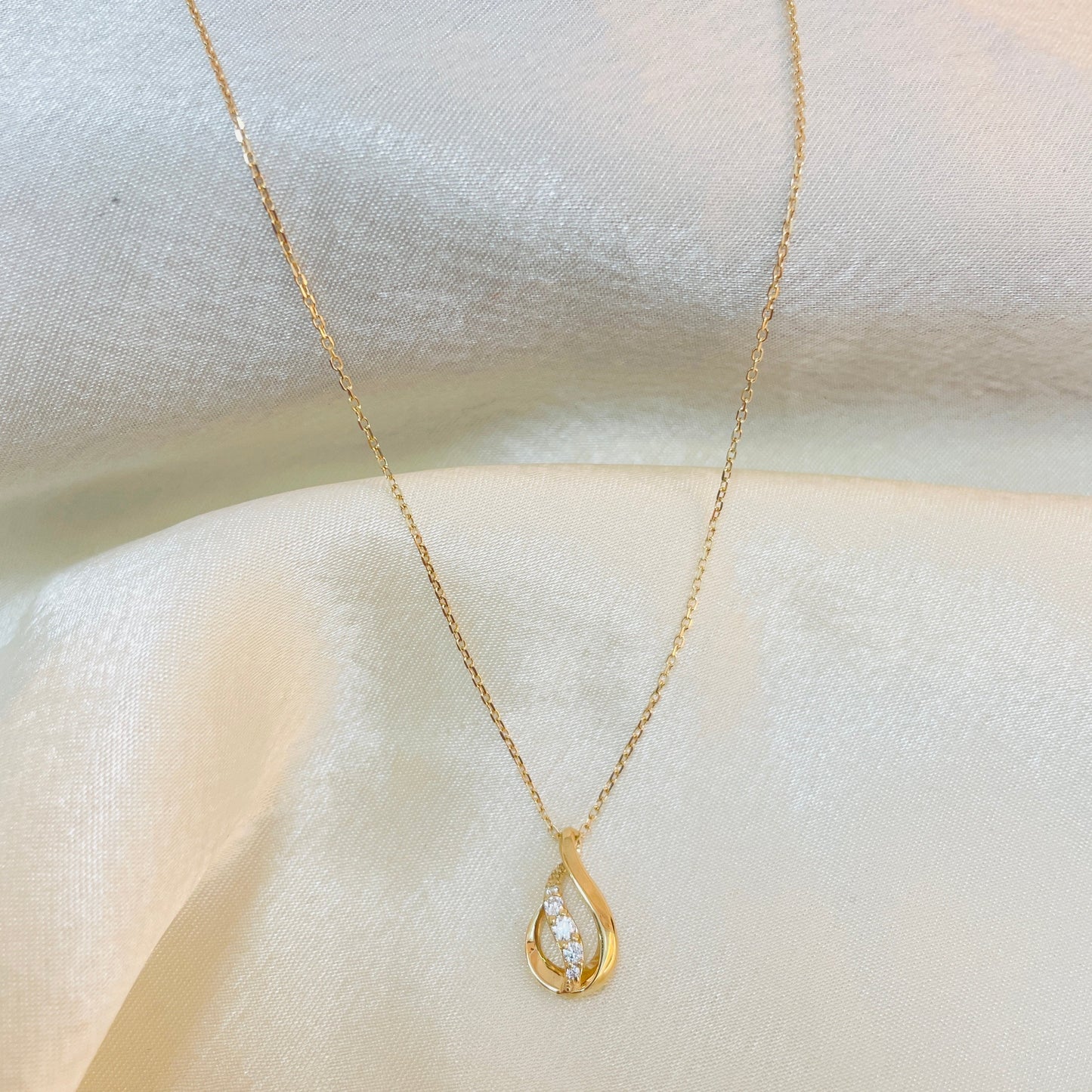 Gold necklace with a teardrop-shaped pendant on a white fabric background
