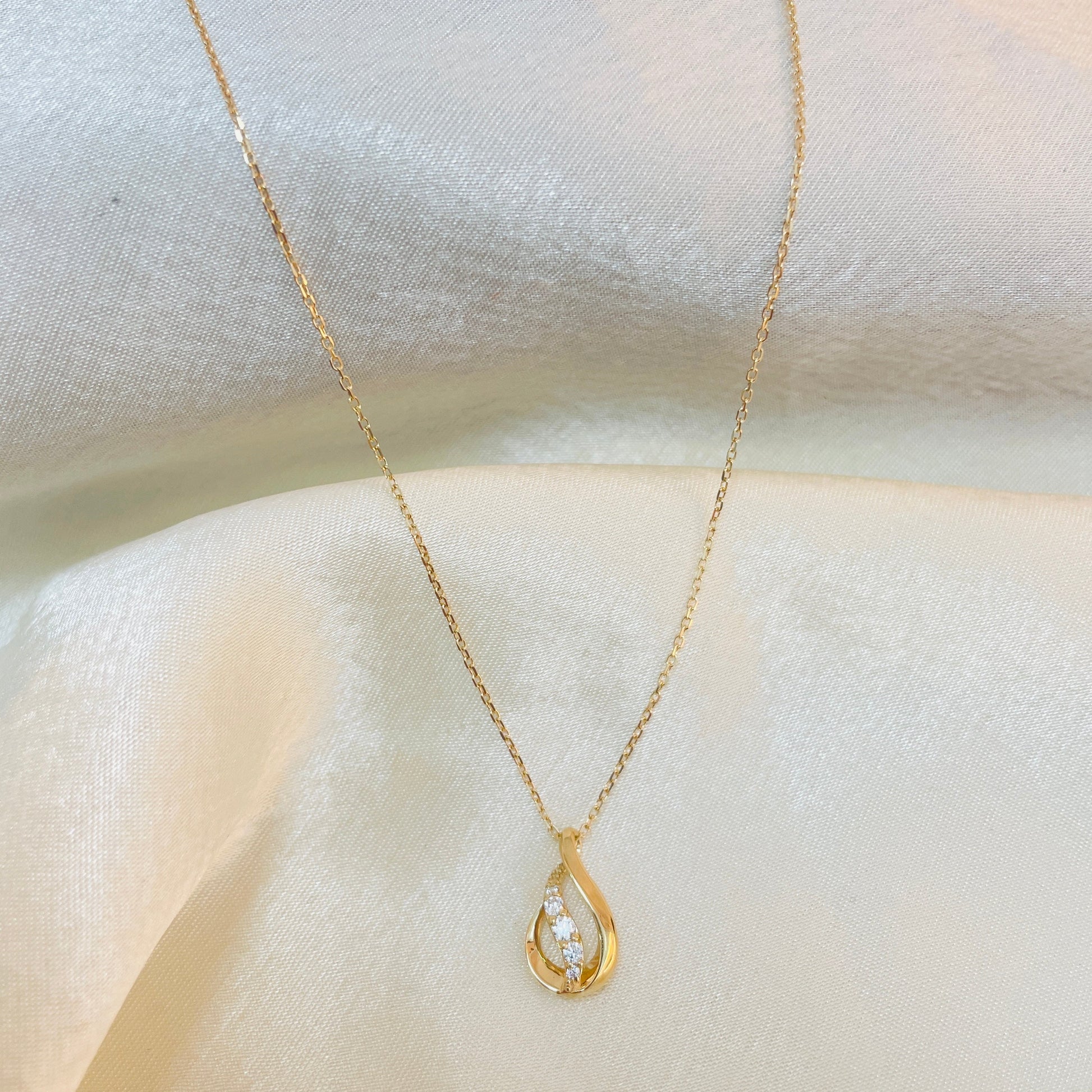 Gold necklace with a teardrop-shaped pendant on a white fabric background
