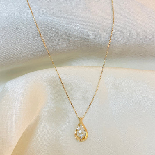 Gold necklace with a teardrop-shaped pendant on a white fabric background