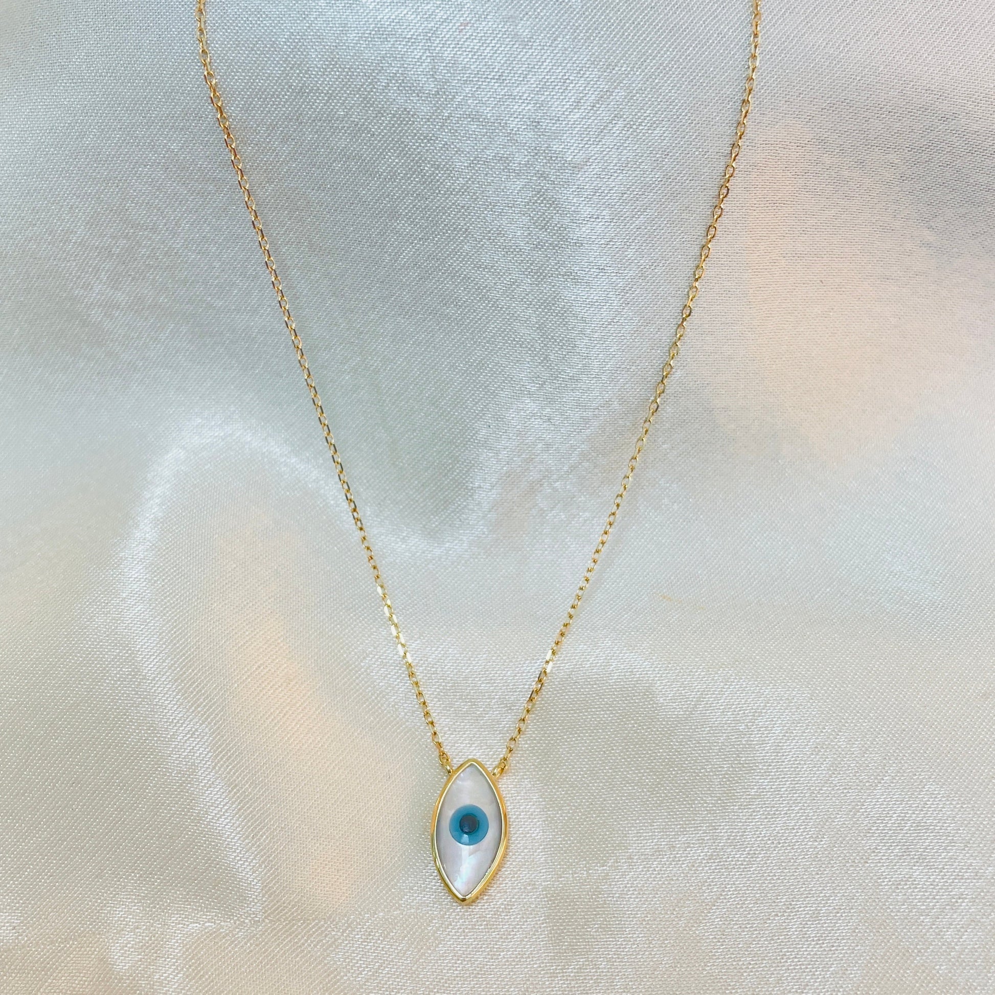 Gold necklace with a blue eye-shaped pendant on a light fabric background