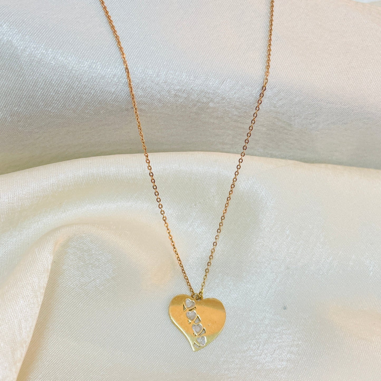 Gold heart-shaped necklace with a pendant on a white fabric background