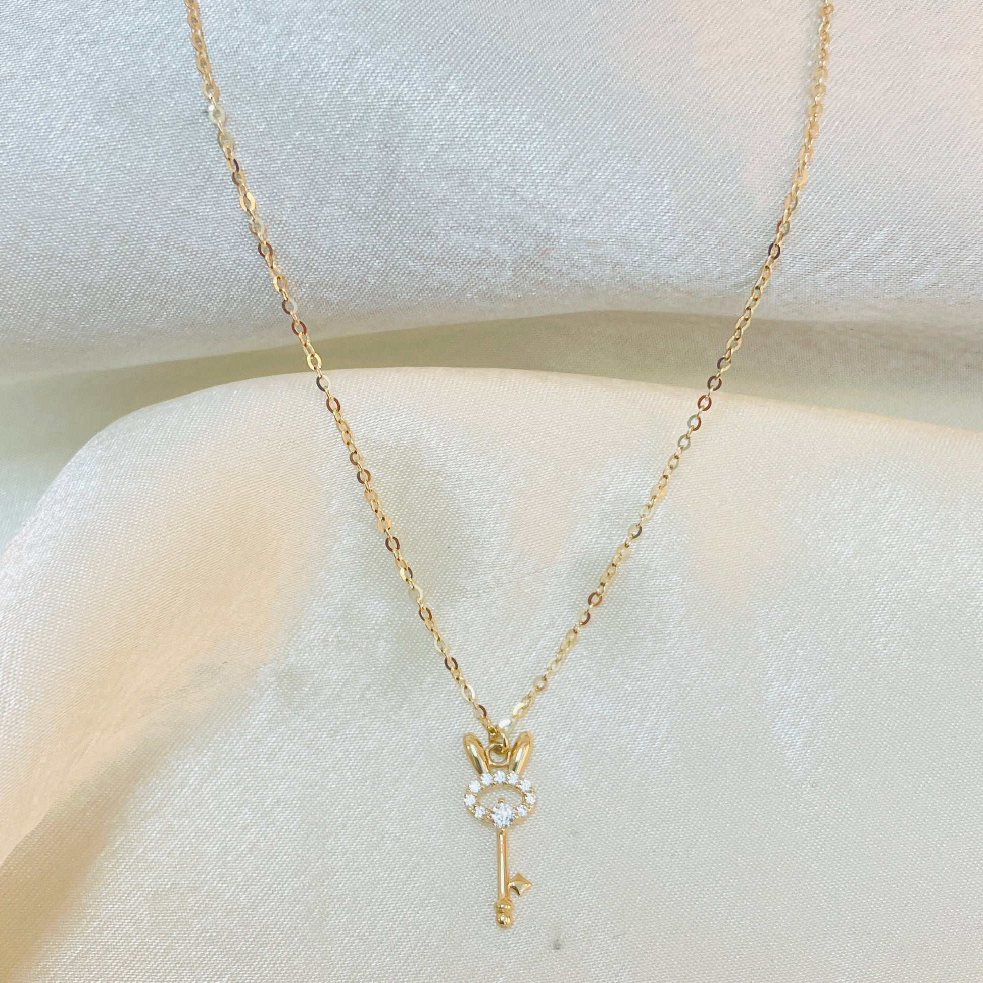 Gold key-shaped necklace with a small pendant on a white surface
