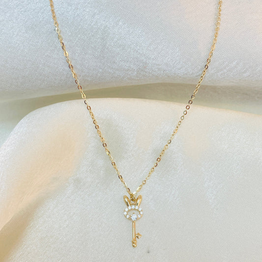 Gold key-shaped necklace with a small pendant on a white surface