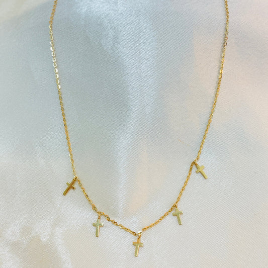 Gold necklace with small cross pendants on a white fabric background