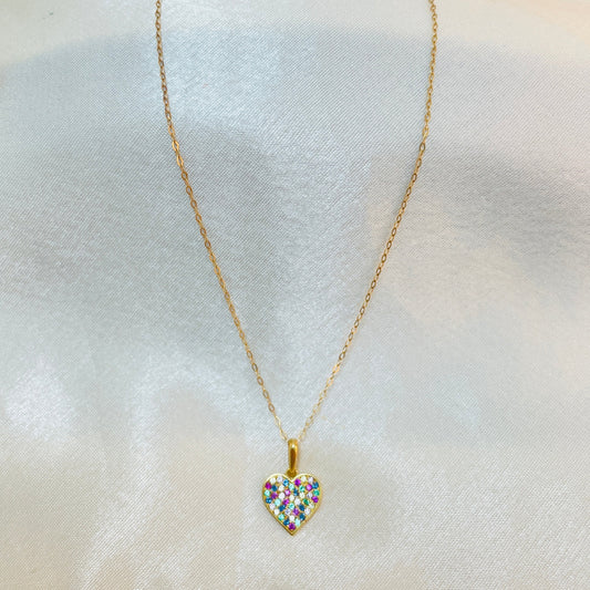 Gold necklace with a heart-shaped pendant featuring colorful stones on a light fabric background