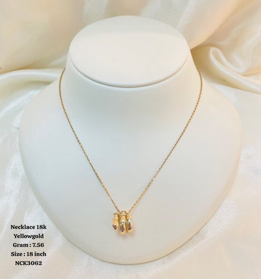 A gold necklace displayed on a white jewelry bust against a soft white fabric backdrop. The pendant consists of three small polished gold bars hanging from a delicate chain.