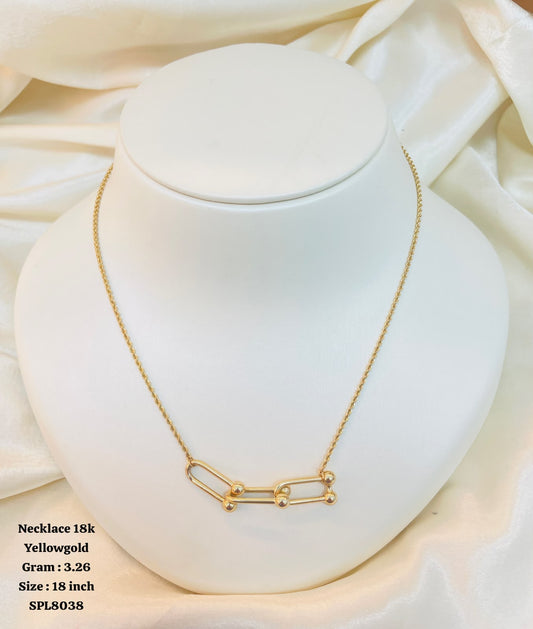 A gold necklace displayed on a white jewelry bust against a soft cream satin background. The necklace has a delicate chain and a pendant made of linked oval shapes with small bead details.
